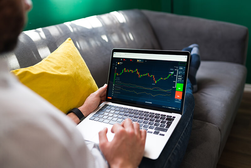 financas comerciais jovem descansando no sofa enquanto verifica o mercado de acoes no laptop