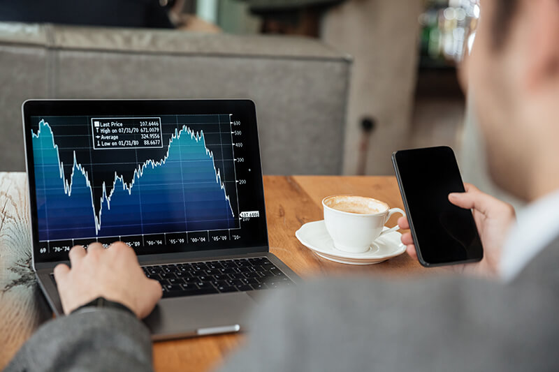 imagem recortada de empresario sentado a mesa no cafe e analisando indicadores no computador portatil enquanto estiver usando o smartphone