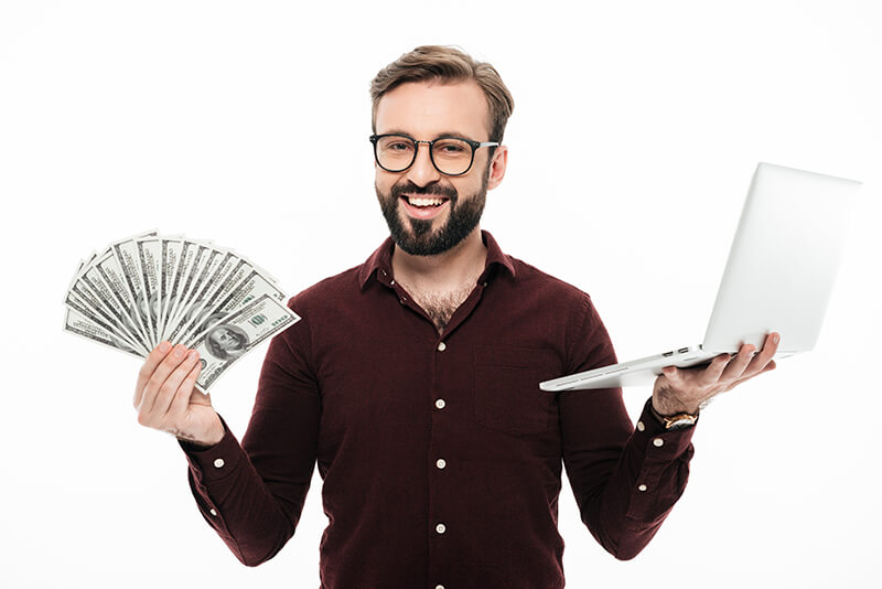 jovem alegre segurando dinheiro e computador portatil