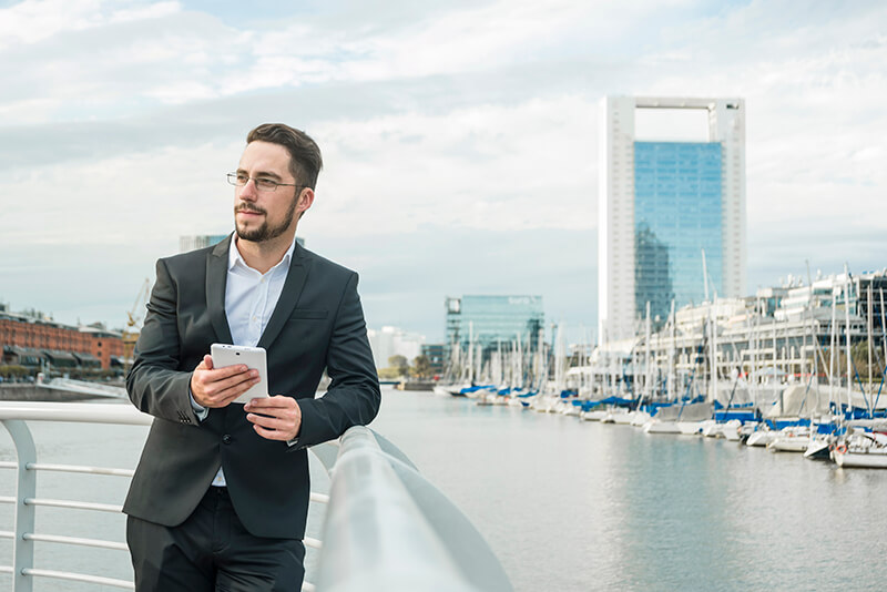 retrato de um jovem homem negocios fica perto porto segurando telefone movel em mao olhando